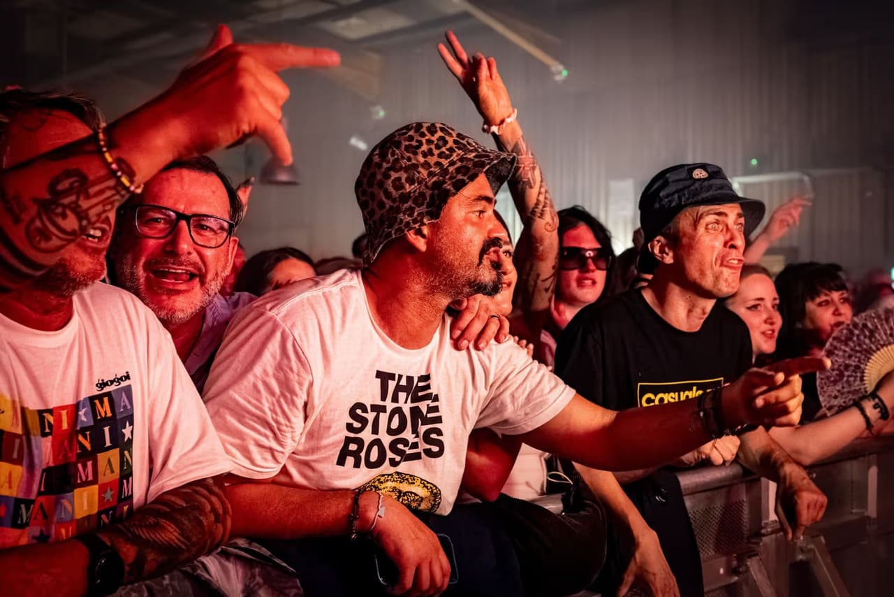 The front row at the barrier: bucket hats, a Stone Roses shirt and hands in the air.