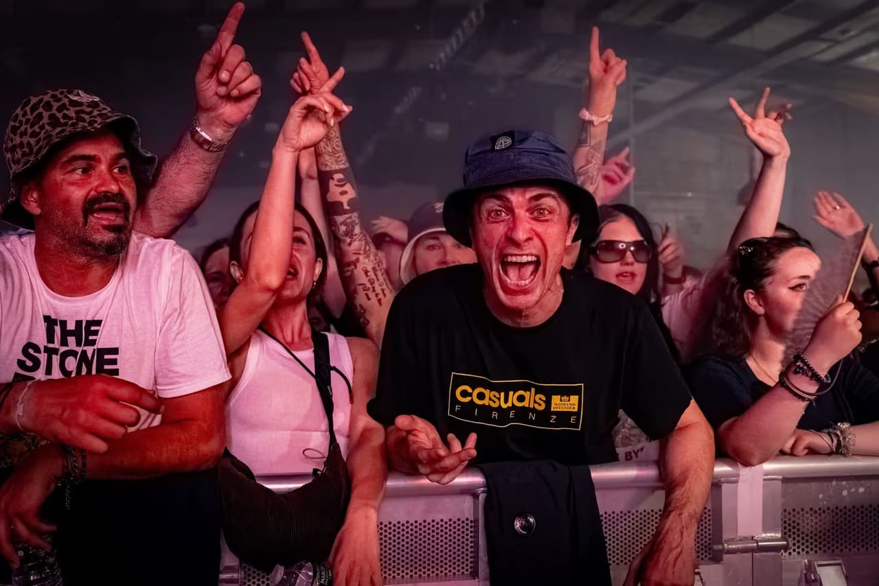 A fan in a bucket hat roars at the barrier, fingers pointing skyward around him.