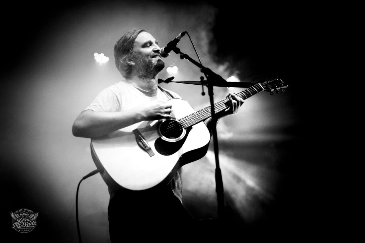 Black and white: an acoustic guitarist singing into the mic through the haze.