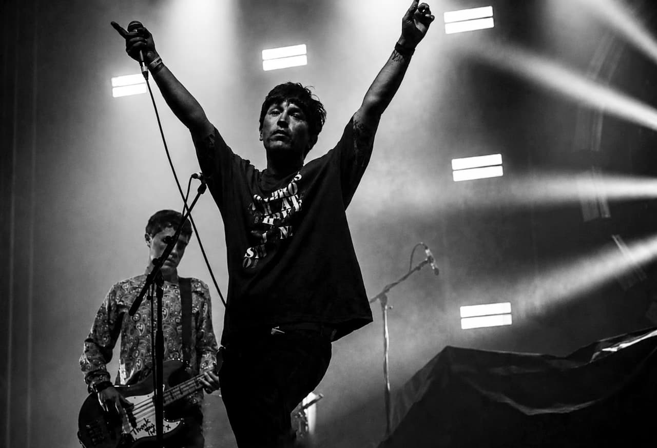 Black and white: a frontman with arms in the air, bassist behind him in a paisley shirt.