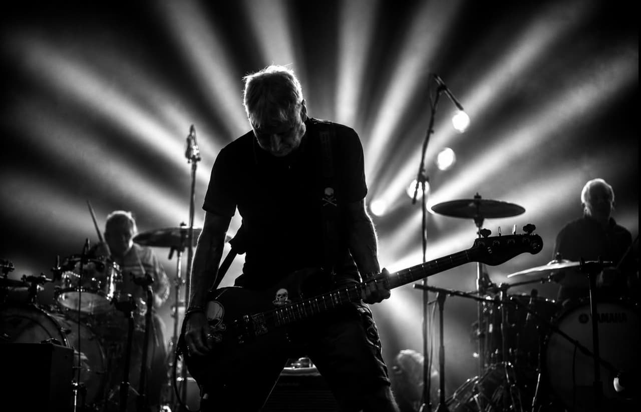 Black and white: a bassist silhouetted against rays of white light, drummers either side.