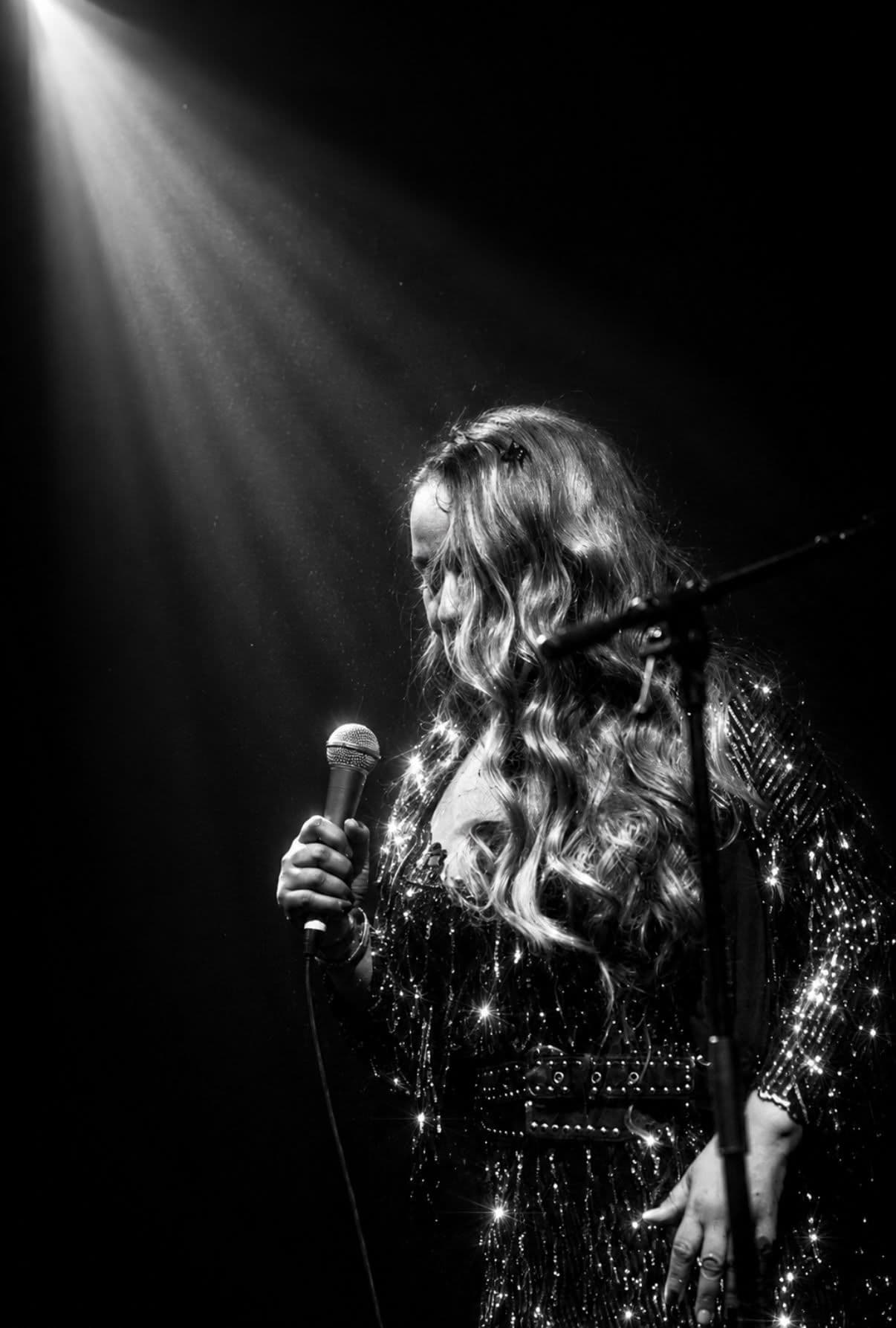 Black and white: a singer in a sequinned jacket under a single beam of spotlight.