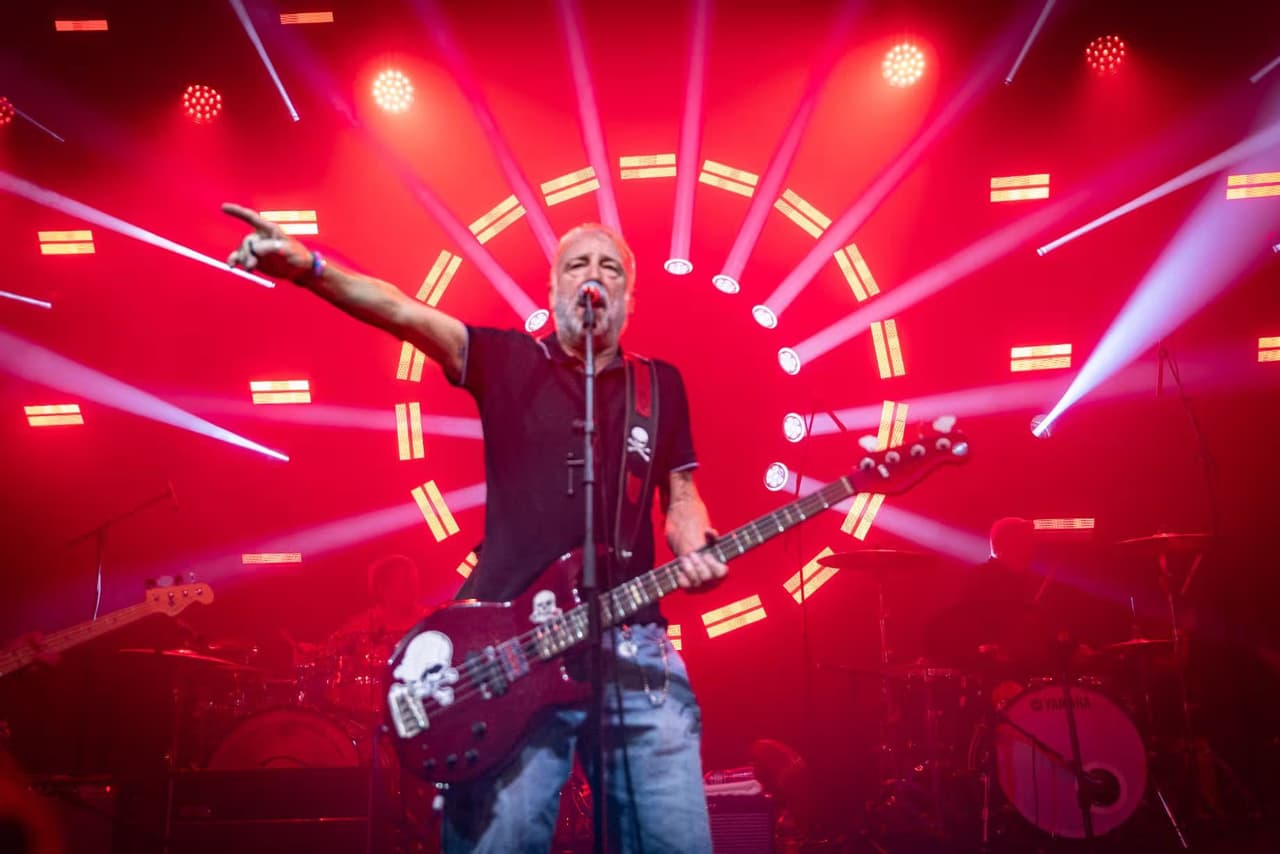 Peter Hook points to the crowd in front of a spiral of red stage lights.