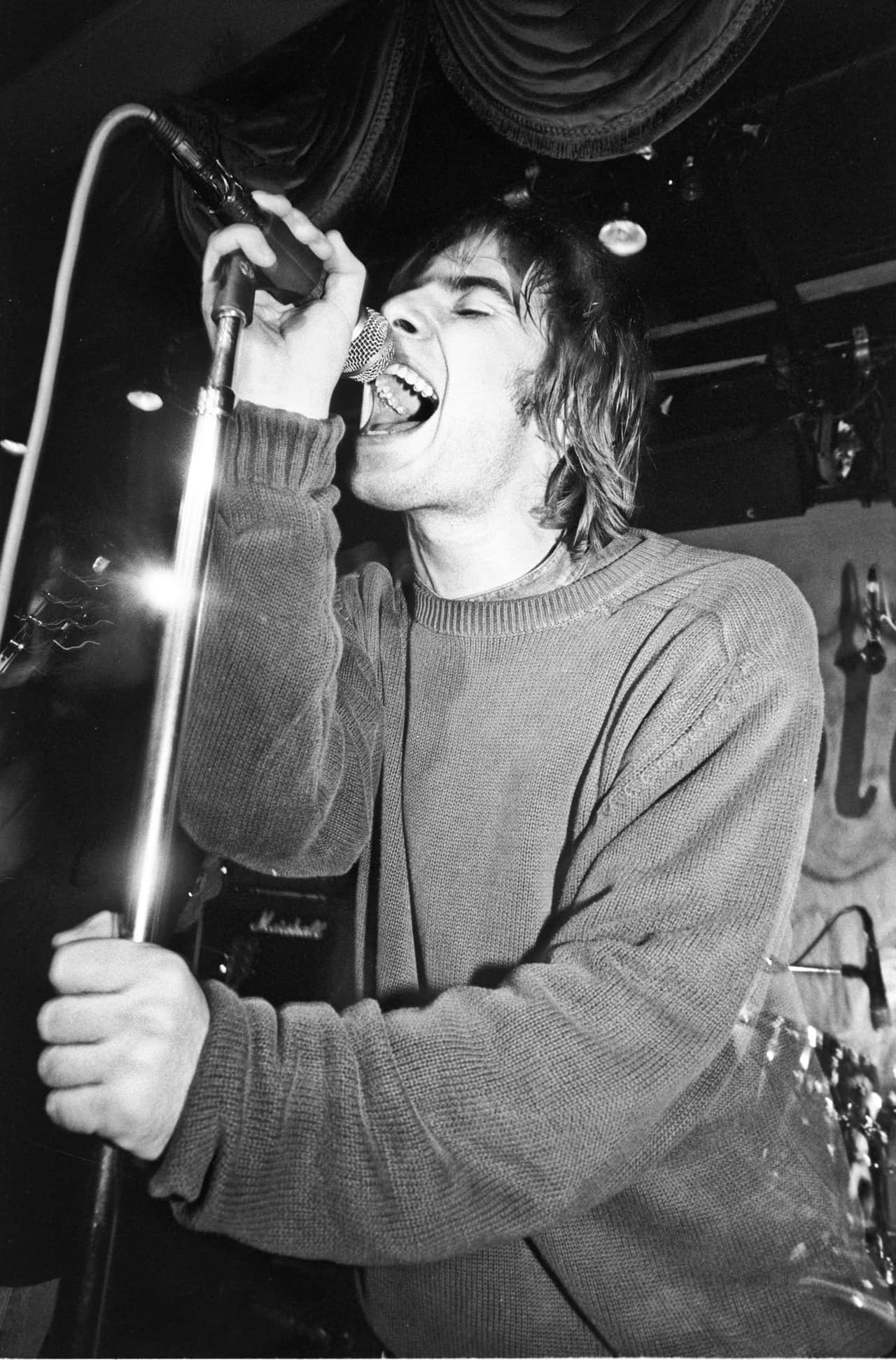 Liam Gallagher roars into the mic in a chunky knitted jumper, black and white.