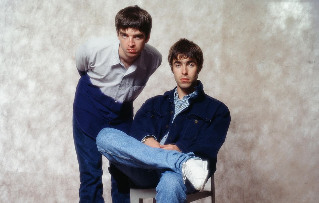 Noel and Liam Gallagher of Oasis in a mid-nineties studio portrait, Liam seated on a chair.
