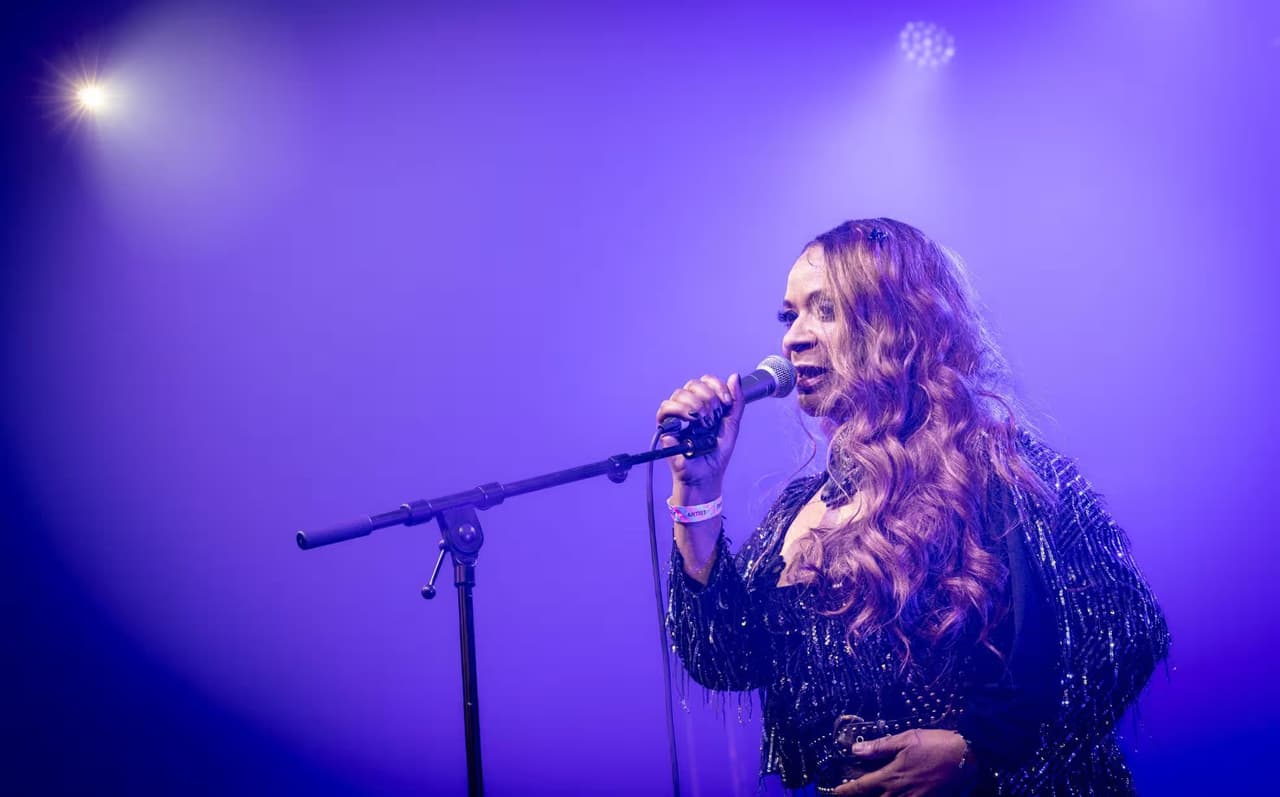 A singer in a sequinned jacket reaches out through purple haze.